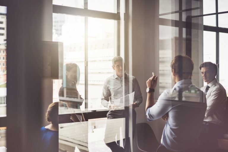 A photo of business people having discussion in board room. Male and female professionals are seen through glass. They are working in office.