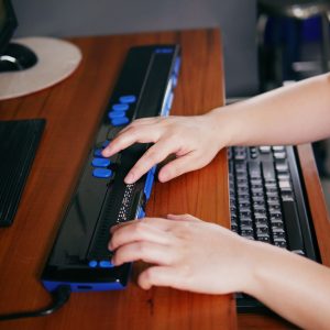 Person with blindness disability's hands using computer with braille display or braille terminal a technology assistive device for persons with visual impairment.