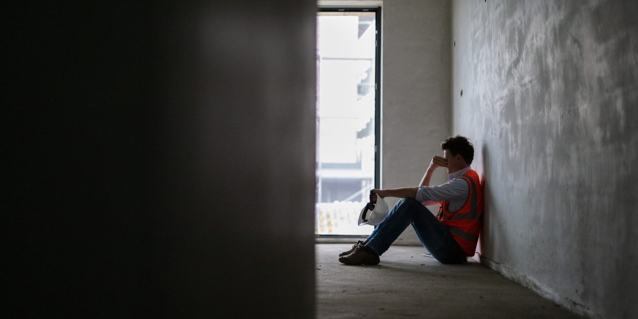 Depressed building contractor sitting inside incomplete house at construction site