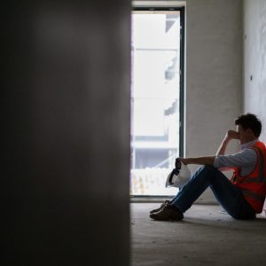 Depressed building contractor sitting inside incomplete house at construction site