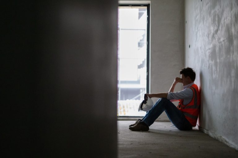 Depressed building contractor sitting inside incomplete house at construction site