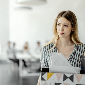 Upset businesswoman with cardboard box of things leaving office after being fired