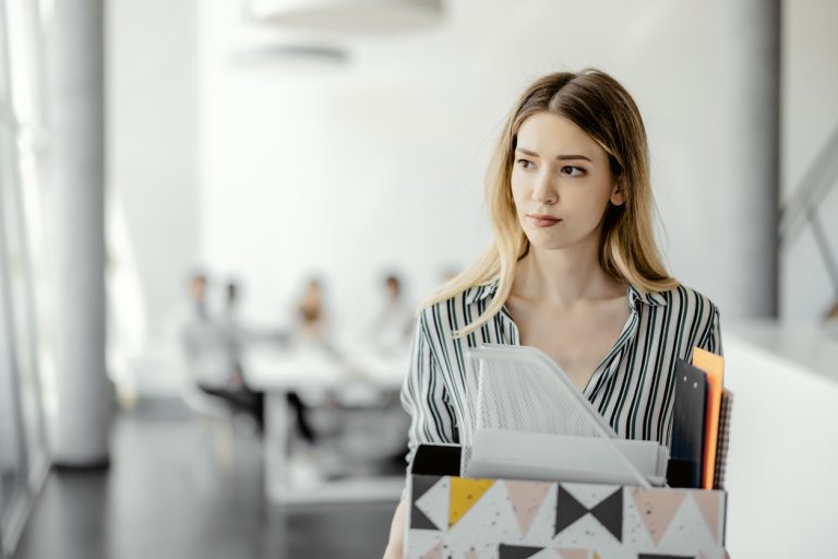 Upset businesswoman with cardboard box of things leaving office after being fired