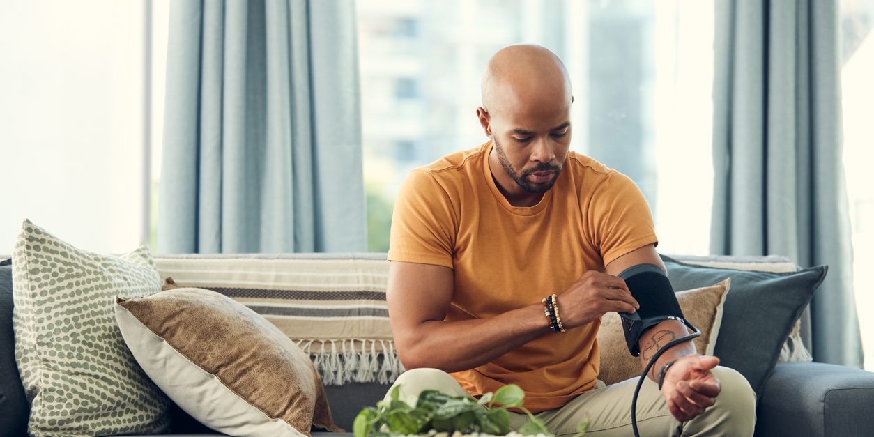 Shot of a young man taking his blood pressure while sitting on the sofa at home