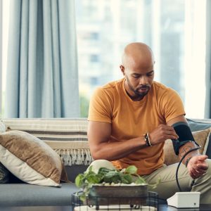 Shot of a young man taking his blood pressure while sitting on the sofa at home