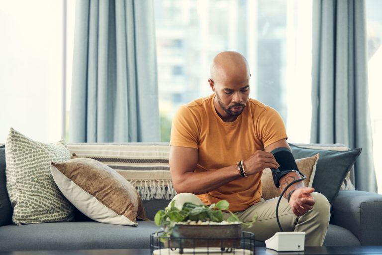 Shot of a young man taking his blood pressure while sitting on the sofa at home